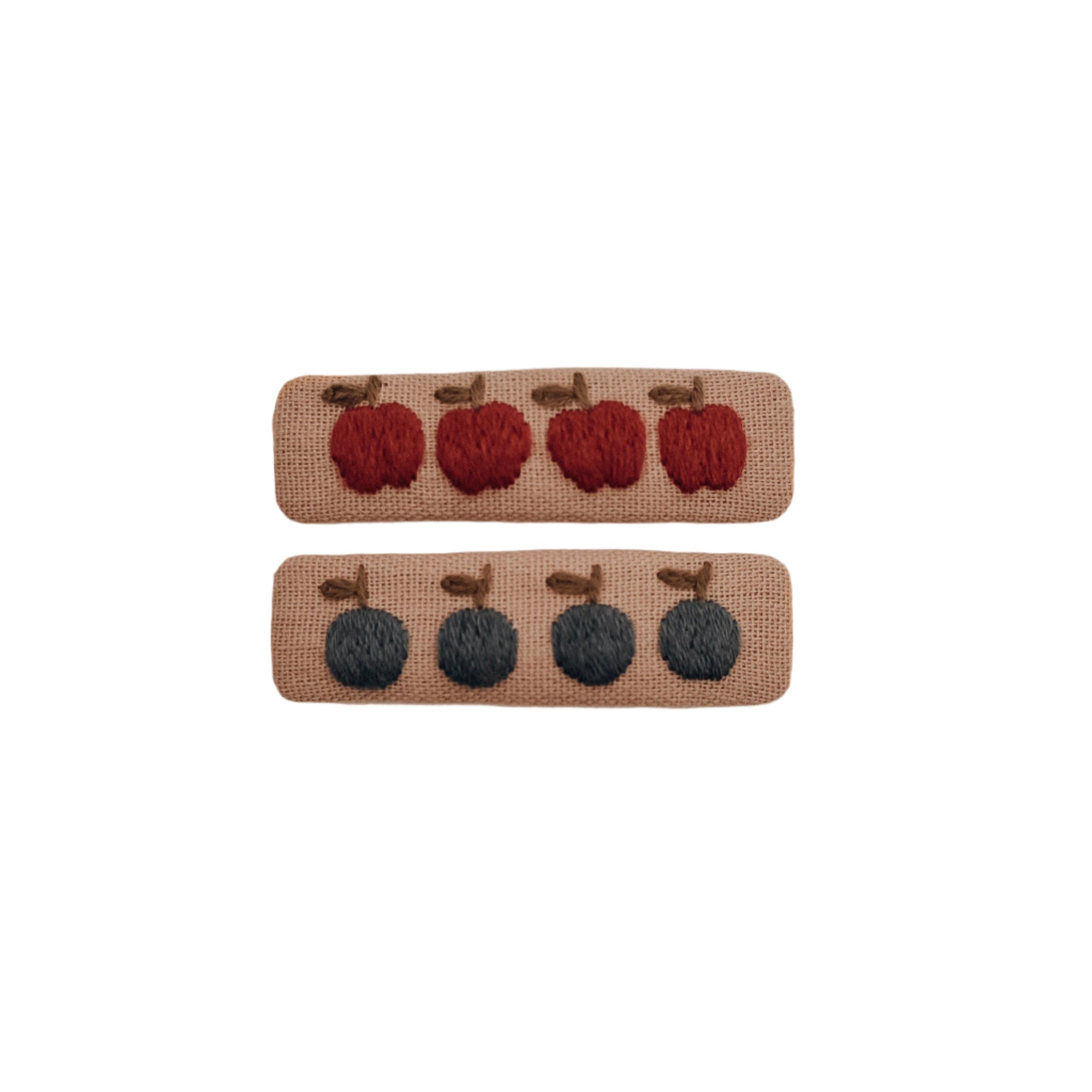 Two linen hair clips embroidered with fruit: one with navy blue berries and the other with red apples, displayed flat on a light neutral background.